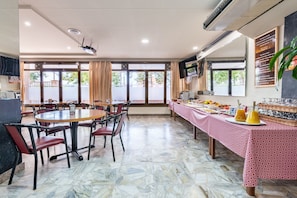 A dining area with a marble floor, round tables, and chairs. There is a buffet table with food and drinks.