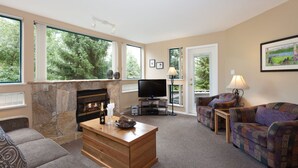 A living room with a stone fireplace, a television, and a sofa. - Greystone #105, Renovated Ski in Ski out, sleeps 5, Free Wifi (105) (Whistler)