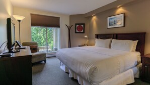 Een hotelkamer met een groot bed, een bureau met computer, een stoel en een raam met jaloezieën.