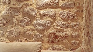A room with a stone wall, a beige sofa, and floral-patterned pillows. - Stoned Traditional House just 3km from amazing beaches (Kalamitsi)