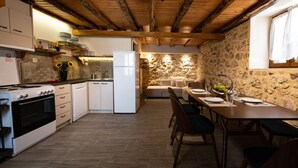 A kitchen with a stone wall, wooden beams, and a dining area with a table set for four. - Stoned Traditional House just 3km from amazing beaches (Kalamitsi)