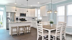 A modern kitchen with white cabinets, stainless steel appliances, and a central island with bar stools. - Spacious Beach Retreat Near VB Boardwalk! (Virginia Beach)