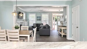A spacious living area with a dining table and chairs, a gray sofa, and a kitchen in the background. - Spacious Beach Retreat Near VB Boardwalk! (Virginia Beach)