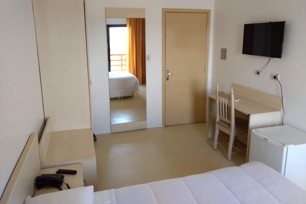 Ein Hotelzimmer mit Bett, Schreibtisch, Stuhl, Fernseher und Kleiderschrank.