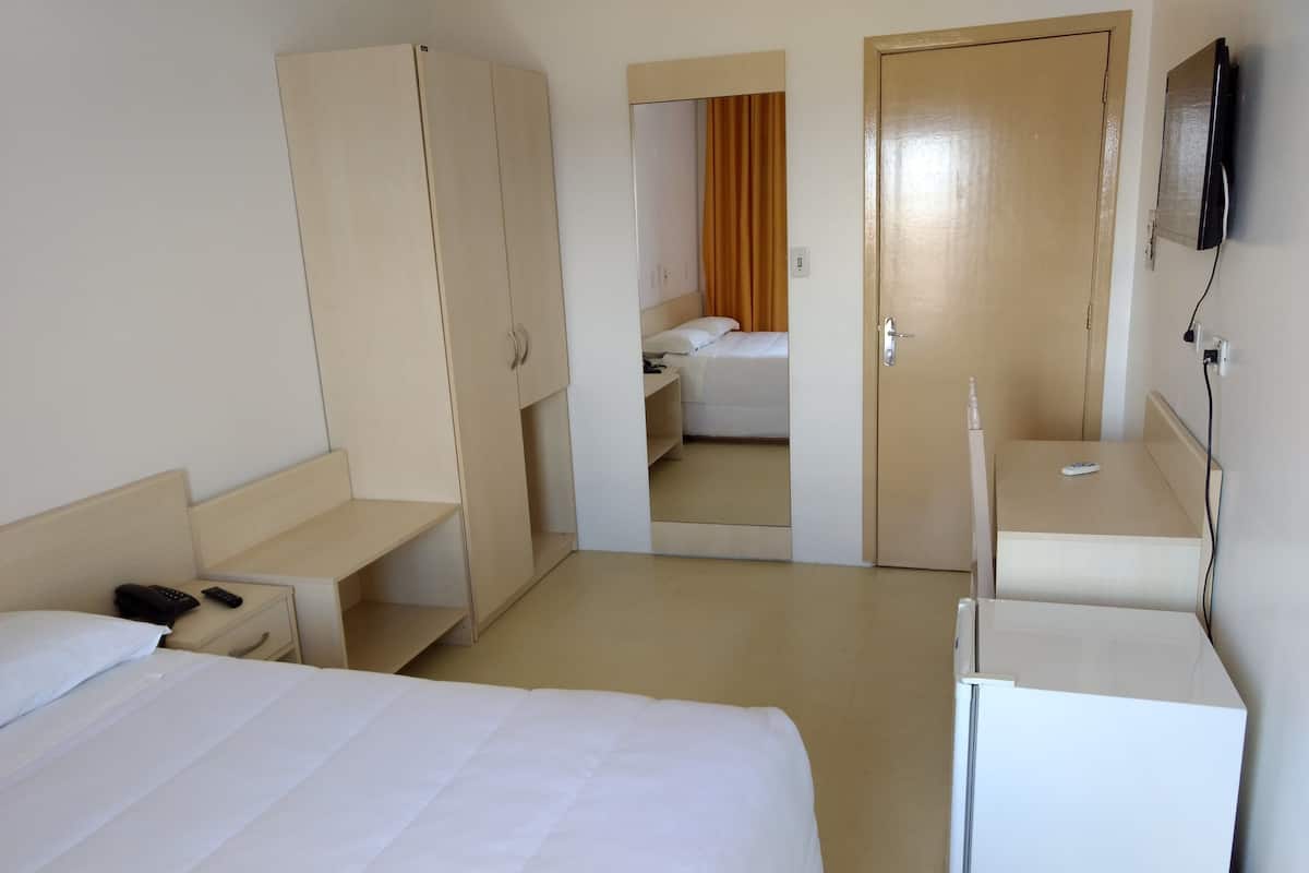 Ein Hotelzimmer mit einem Bett, einem Schrank, einem Schreibtisch, einem Spiegel und einem Fernseher.