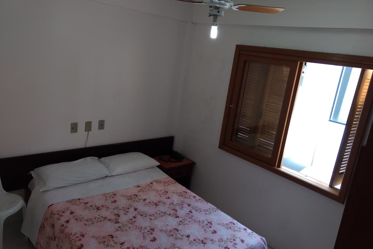 Ein Schlafzimmer mit einem Bett, einem Nachttisch, einem Deckenventilator und einem Fenster mit Jalousien.