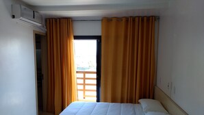 A hotel room with a bed, curtains, an air conditioning unit, and a view through the window. - Hotel Kimar (Tramandai)