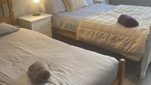 Ein Hotelzimmer mit zwei Betten, jeweils mit einem Holz-Kopfteil, einem Nachttisch mit Lampe und einem Fenster mit Vorhängen.