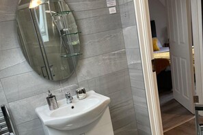 Ein Badezimmer mit einem weißen Waschbecken, einer Duschkabine aus Glas und einem Spiegel.