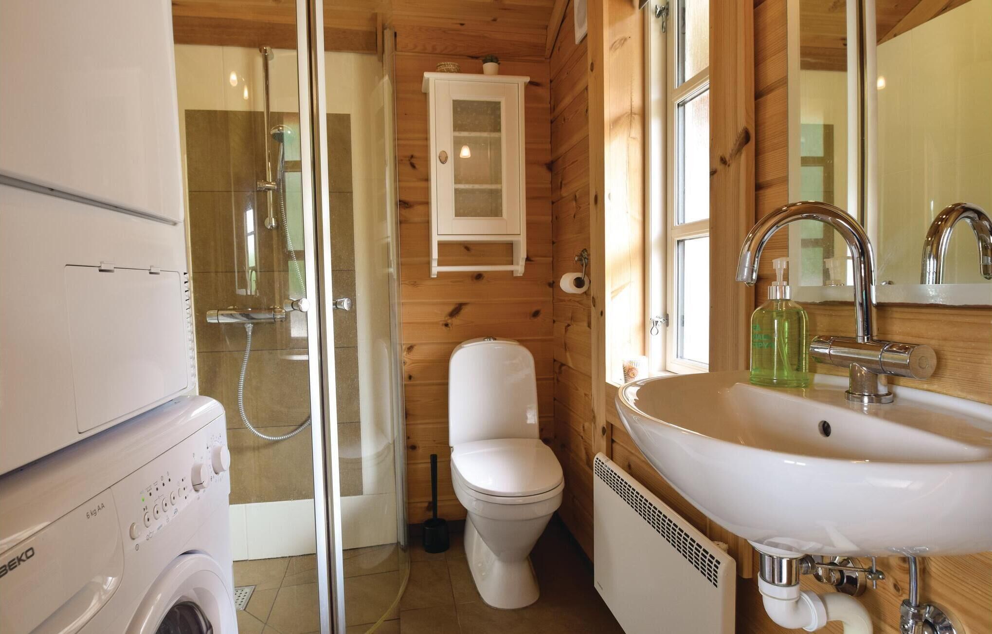 Un baño pequeño con ducha envuelta en vidrio, inodoro, lavabo con espejo y lavadora.
