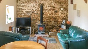 A cozy living room with a stone wall, a fireplace, a television, a green leather sofa, and a wooden table. - 1 bedroom nice home in Fougerolles Du Plessis (Fougerolles Du Plessis)