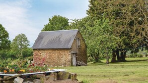A stone cottage with a sloped roof, surrounded by a well-maintained garden with various plants and flowers. - 1 bedroom nice home in Fougerolles Du Plessis (Fougerolles Du Plessis)
