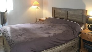 A bedroom with a wooden headboard, a single bed with a grey bedspread, a bedside table with a lamp, and a nightstand with a lamp. - 1 bedroom nice home in Fougerolles Du Plessis (Fougerolles Du Plessis)