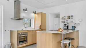 A modern kitchen with wooden cabinets, a built-in oven, a large window, and a coffee machine.