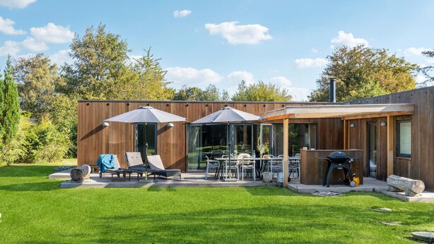 A modern house with a patio area featuring a table, chairs, and a barbecue grill.