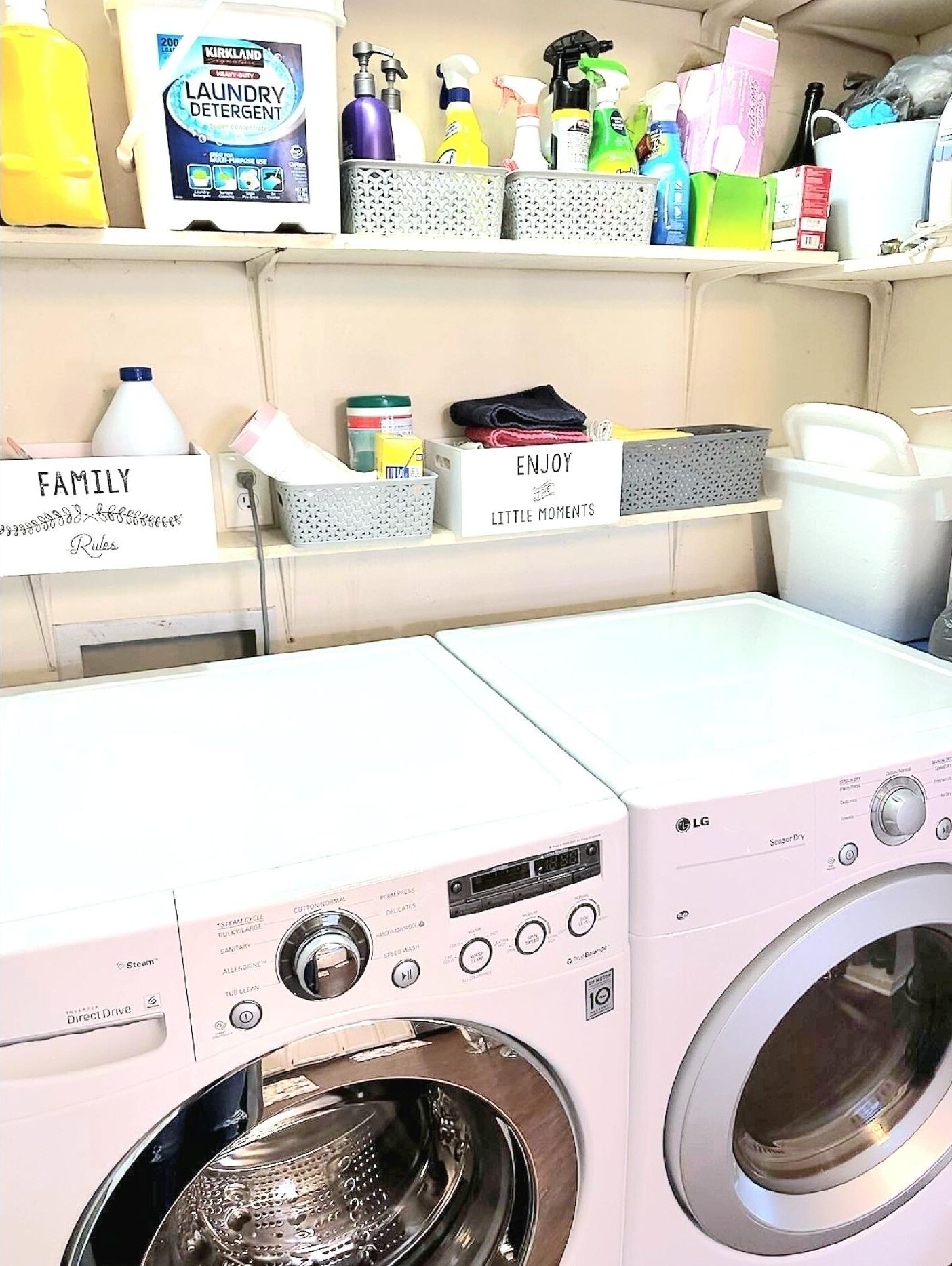 Une buanderie équipée de deux machines à laver LG à entraînement direct, d’étagères contenant divers produits de lessive et d’un panneau indiquant « RÈGLES FAMILIALES ».
