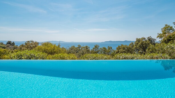 Une piscine d’eau cristalline, d’un bleu éclatant, offrant une vue sur la mer et les collines lointaines.