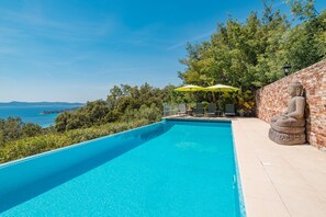 A swimming pool with a view of the sea, a Buddha statue, and a brick wall.
