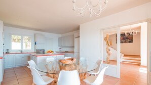 Une cuisine moderne avec des meubles blancs, une table à manger en verre et des chaises blanches.