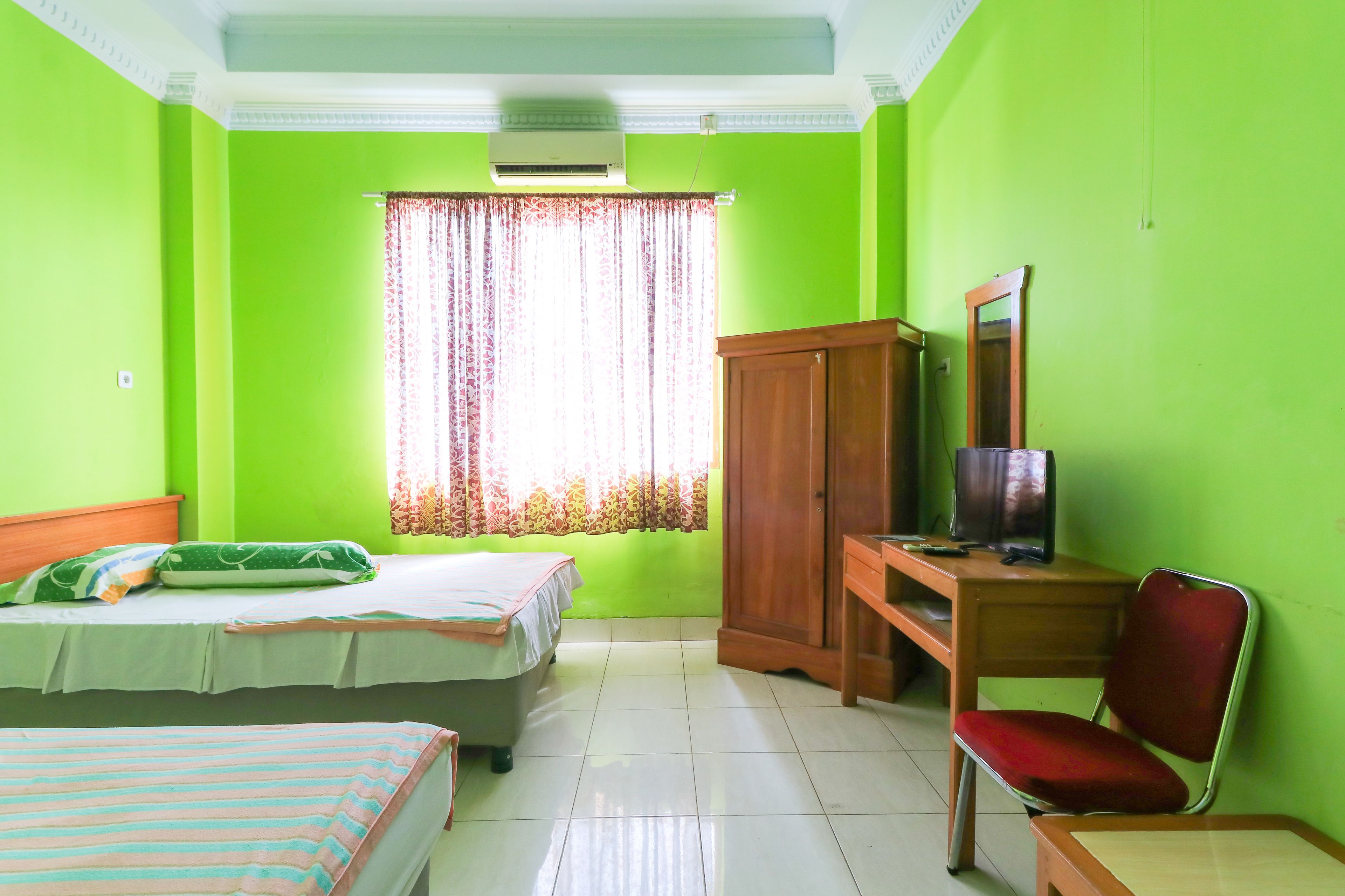 A room with two beds, a desk with a chair, a wardrobe, and a window with curtains.