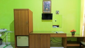Ein Zimmer mit einem Holfischschrank, einem Schreibtisch mit Computer, einem kleinen Waschbecken und einer grünen Wand.