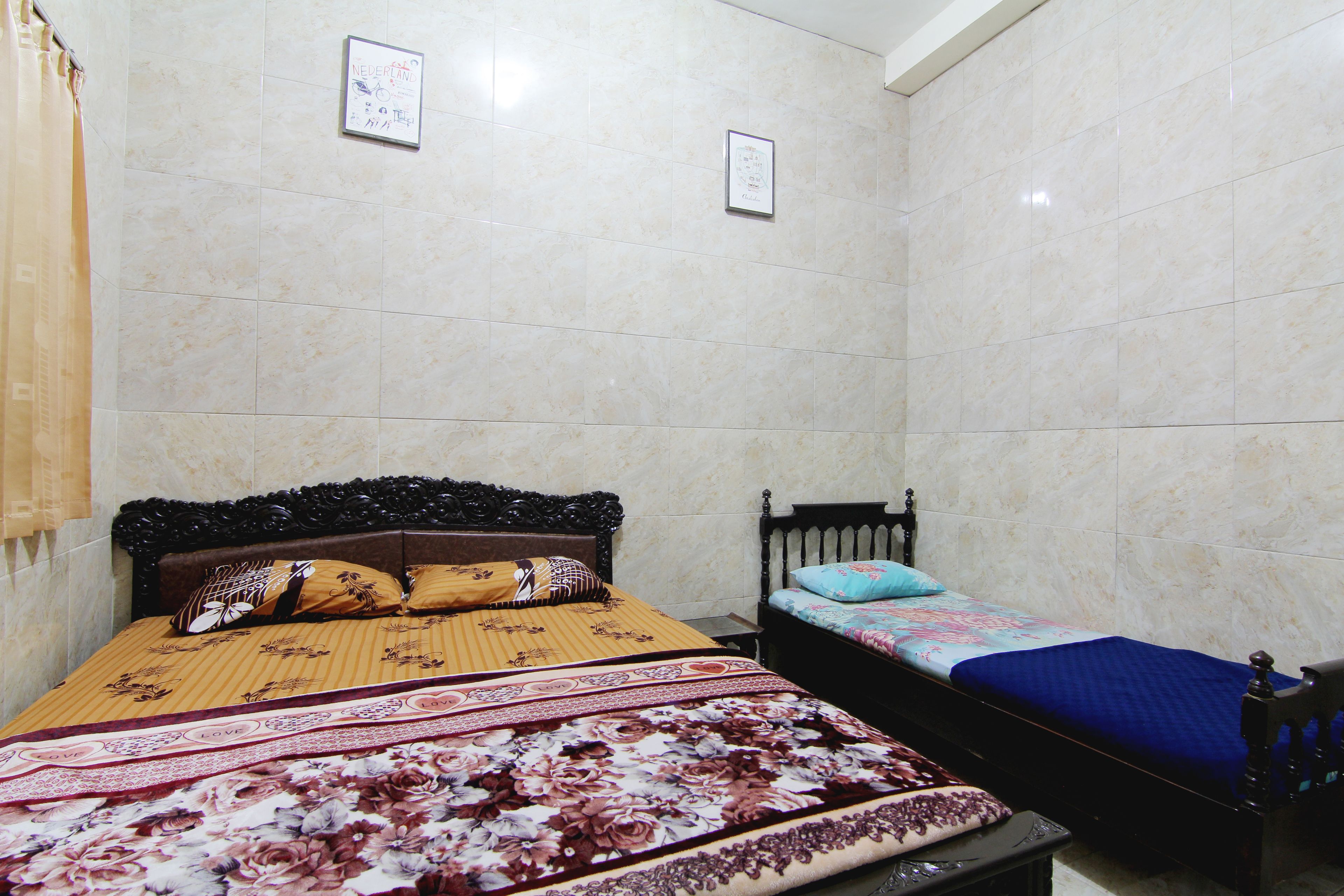 A bedroom with two beds, a large bed with a floral bedspread and a smaller bed with a blue bedspread.