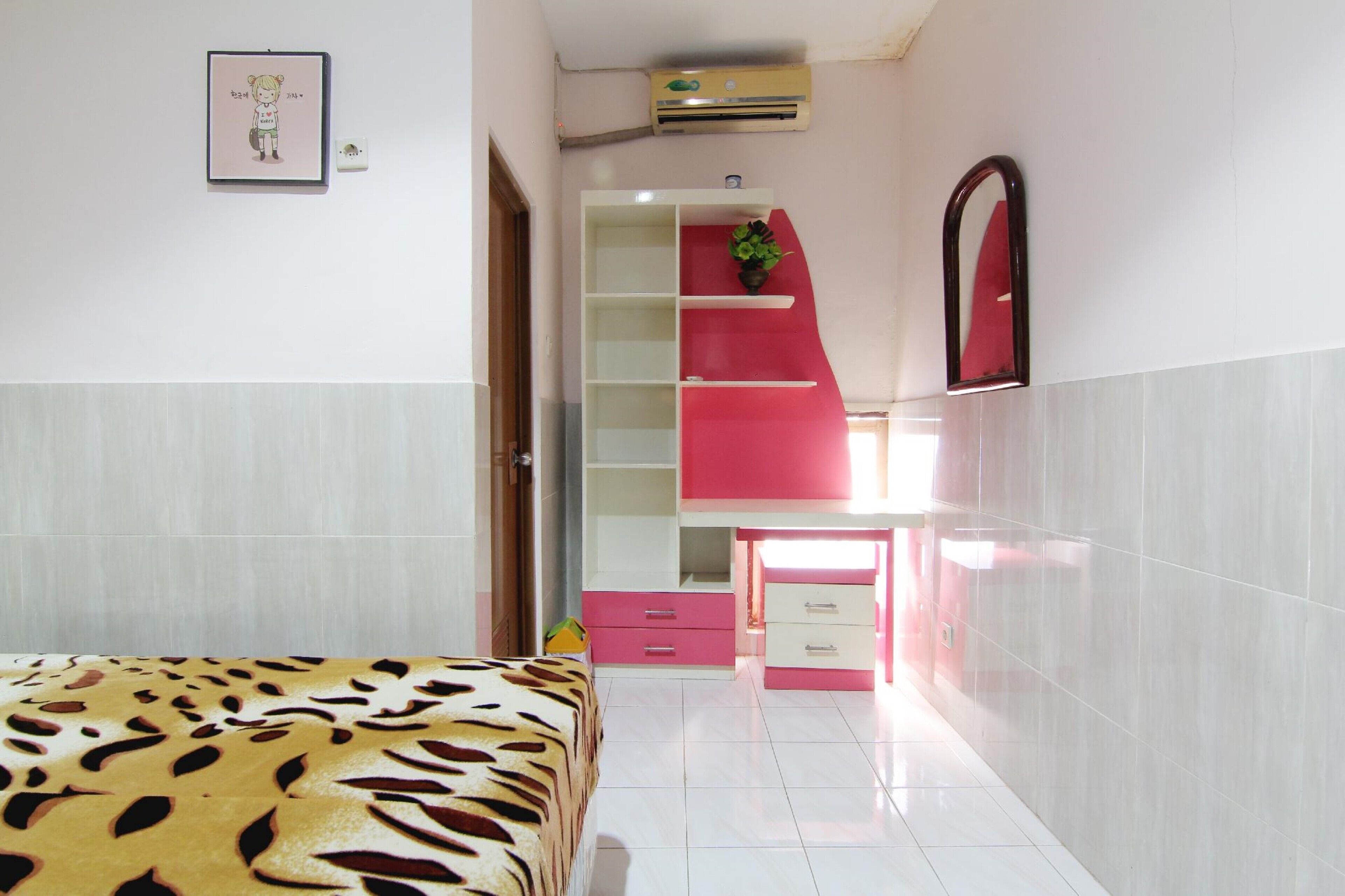 Une chambre avec un lit, un bureau et une chaise. Il y a un miroir au mur et une étagère avec une plante.
