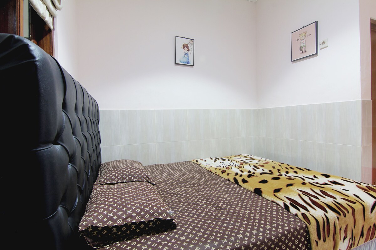 Ein Schlafzimmer mit einer gesteppten Kopfteil, einem Bett mit gemusterten Bettwaren und zwei gerahmten Bildern an der Wand.