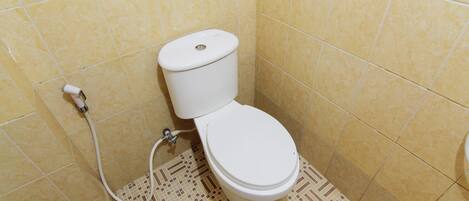 A small bathroom with a toilet, a shower hose, and patterned floor tiles.