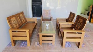 A room with a wooden sofa set around a glass coffee table, a small cabinet, and patterned floor tiles. - Losmen Alden (Parangtritis)