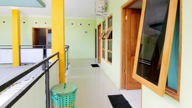 A corridor with a green wall, yellow pillars, and a window with a wooden frame. - Losmen Alden (Parangtritis)