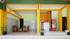 A covered outdoor seating area with wooden chairs and tables, a vending machine, and potted plants. - Losmen Alden (Parangtritis)