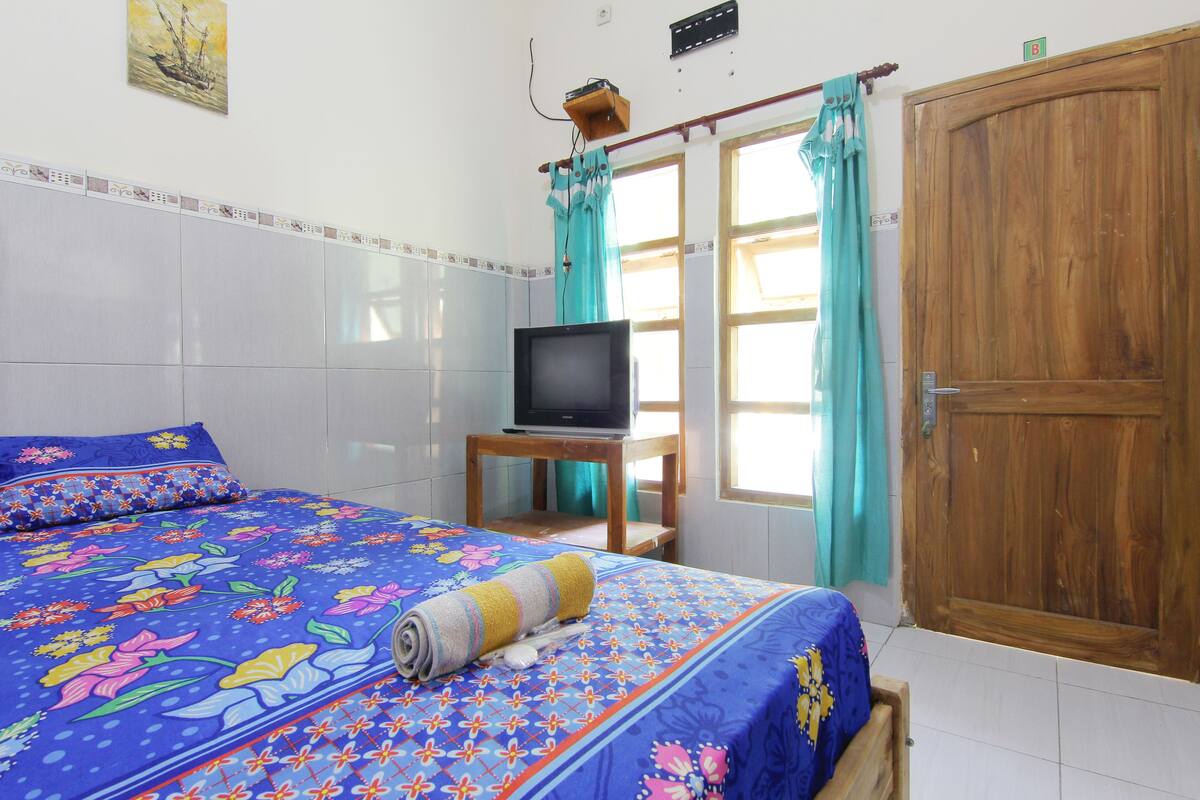 A bedroom with a bed, a television on a small table, and a wooden wardrobe.