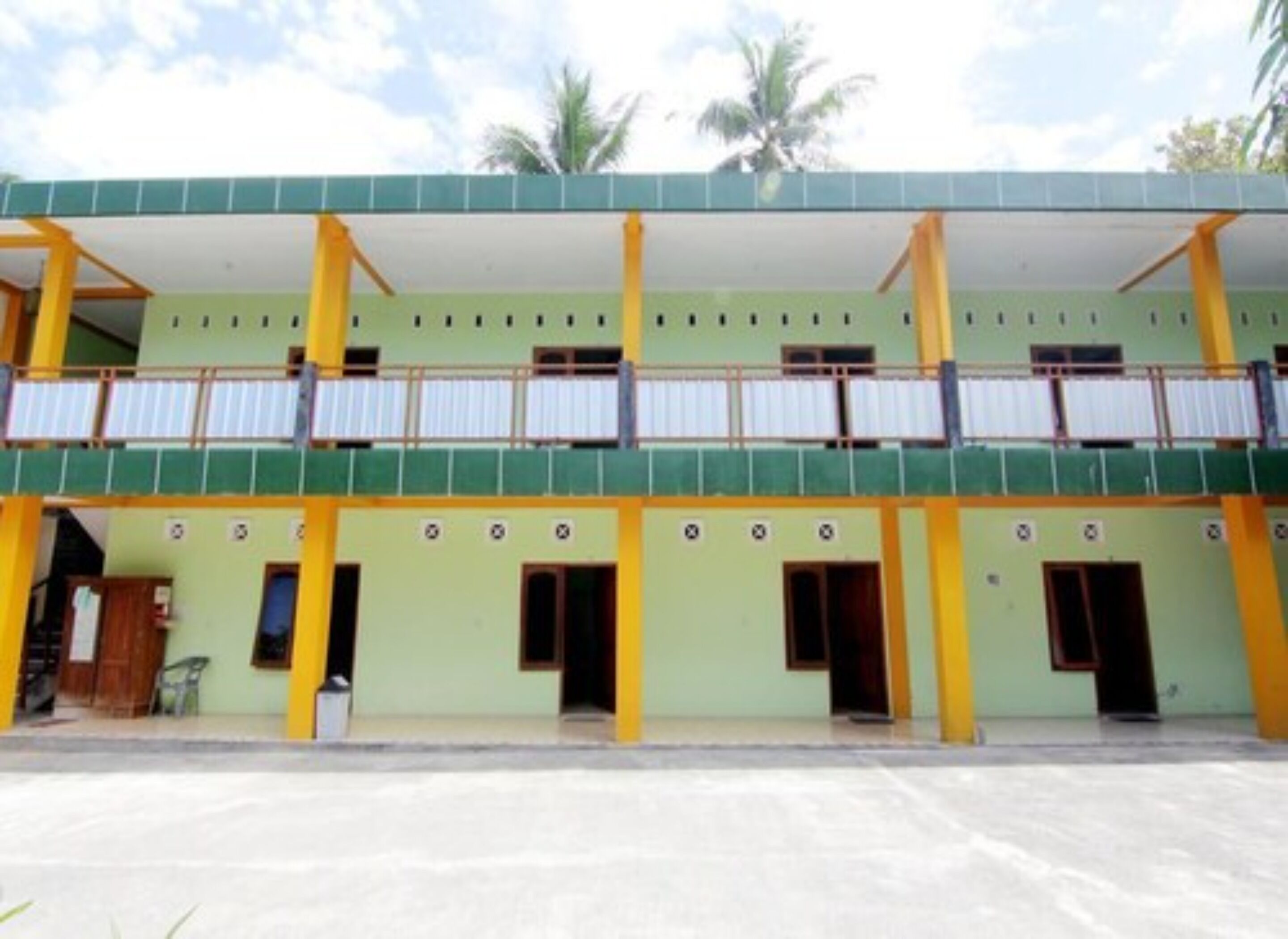 A two-story building with a green and yellow color scheme, featuring balconies and multiple doors.