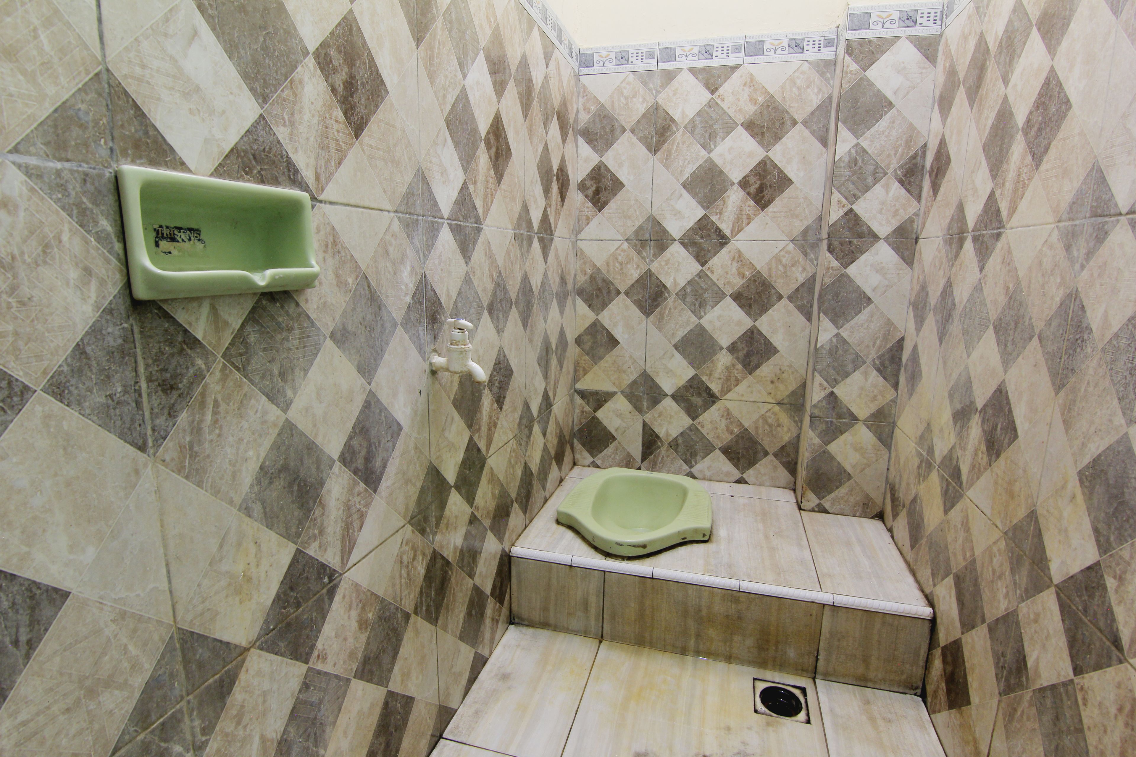 A small bathroom with a green urinal, a toilet, and a shower area with a tiled floor.