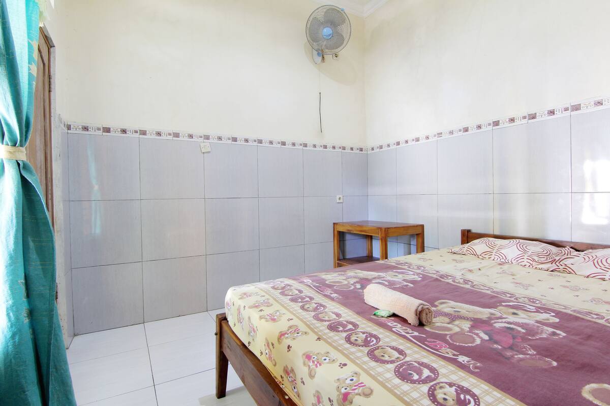 A bedroom with a bed, a small wooden table, and a ceiling fan.