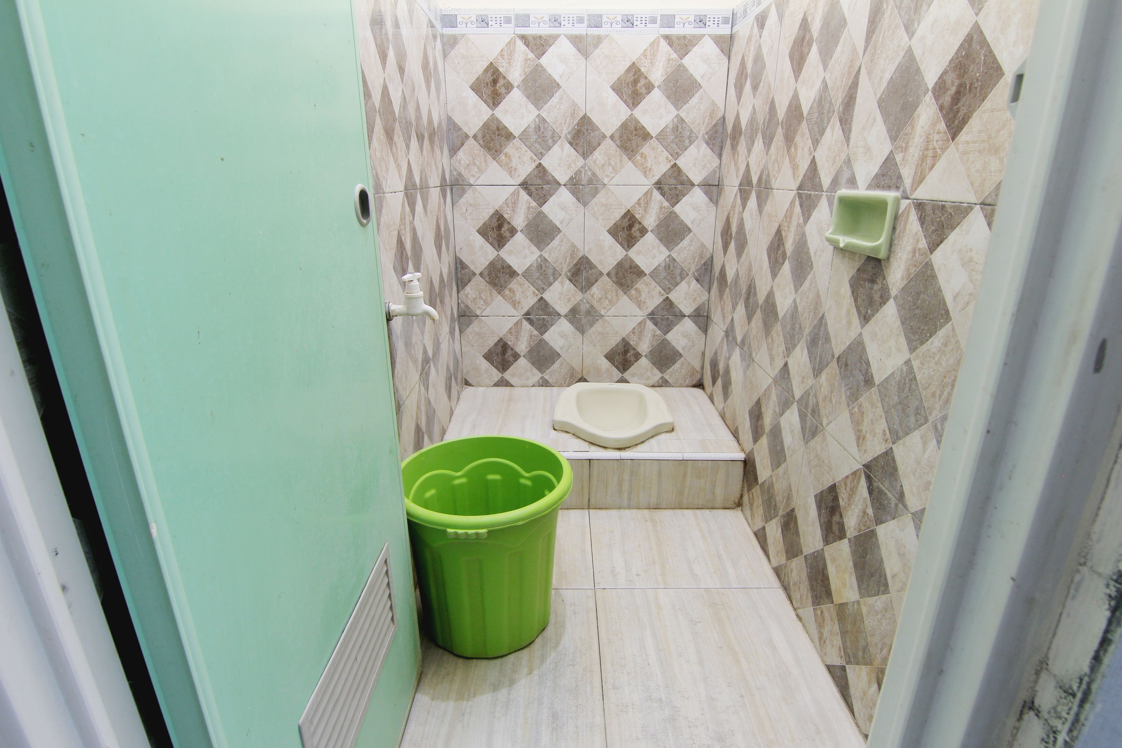Un baño pequeño con inodoro, un cubo de basura verde y suelo de baldosas.