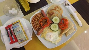Ein Teller Frühstück mit Bohnen, Eiern, Tomaten, Gurken und Toast, zusammen mit einer Tasse und einer kleinen Schale Zuckerwürfeln.