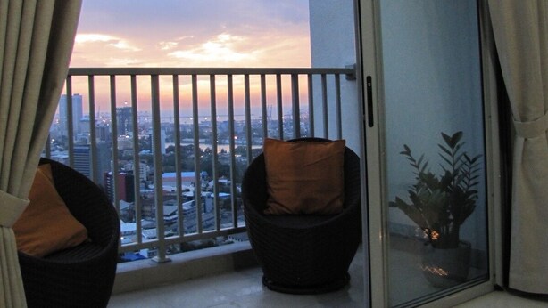 Un balcón con dos sillas, una puerta corrediza de vidrio y vistas a la ciudad al atardecer.