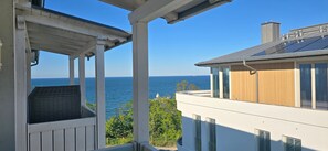 Un balcon avec vue sur la mer, un immeuble moderne avec un revêtement en bois et un ciel d’un bleu éclatant.