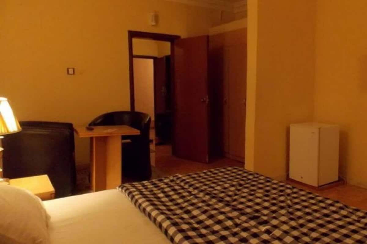 A hotel room with a bed, a desk, a chair, and a small refrigerator.