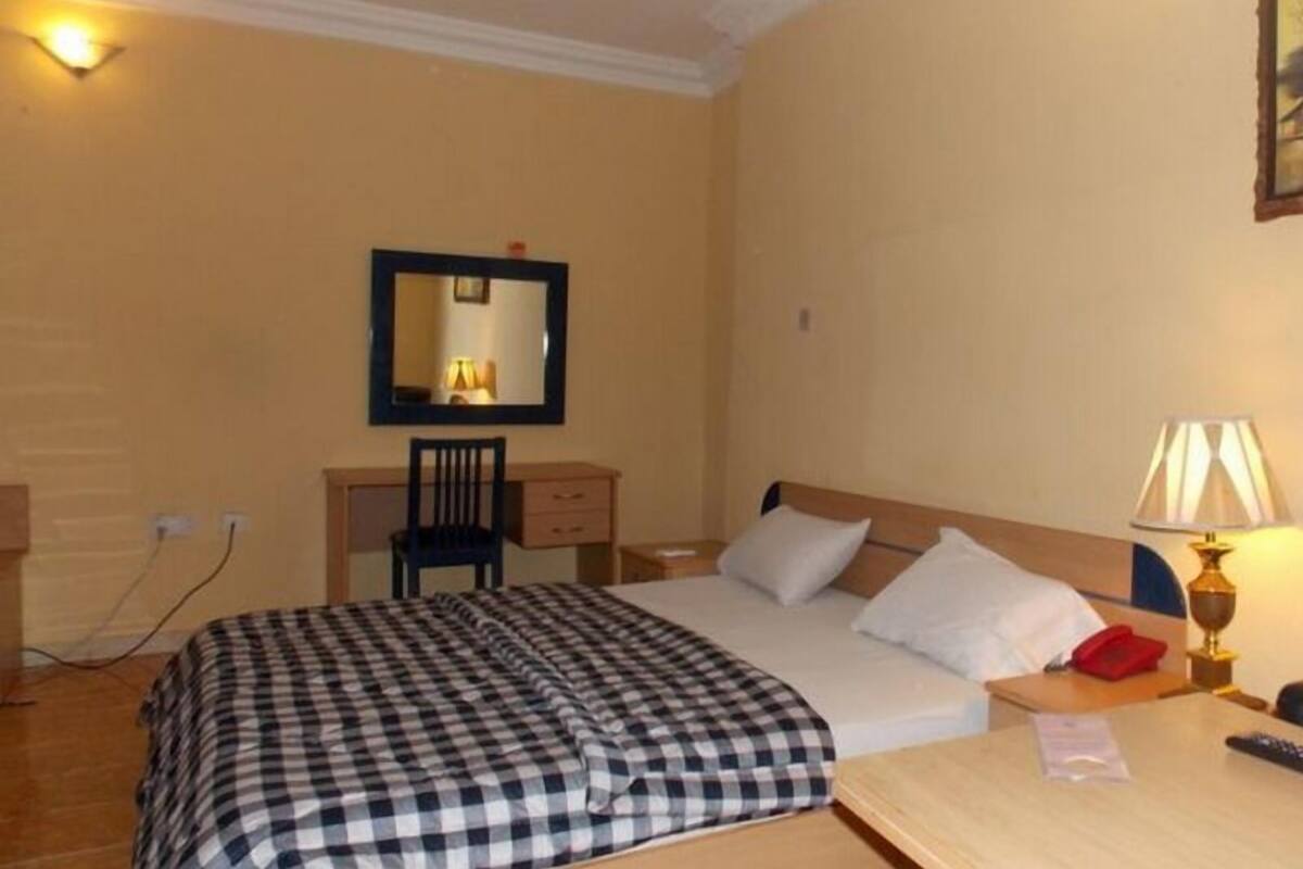 A hotel room with a bed, bedside table, lamp, chair, desk, and a mirror on the wall.