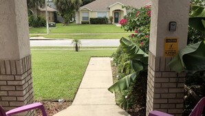 A covered patio with two purple chairs, a pathway leading to a house, and a caution sign indicating a potentially slippery floor. - Robin's Nest- Orlando Villa Vacation Rental. (Clermont)