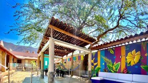 An outdoor patio area with a wooden pergola, a colorful mural, and a seating area. - Hostal  Aurora - Hostel (Santa Marta)