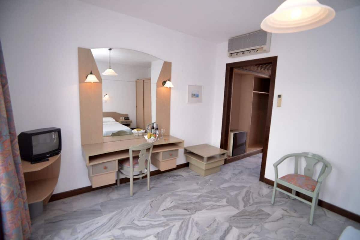 A hotel room with a bed, a desk, a chair, a television, and a wardrobe.