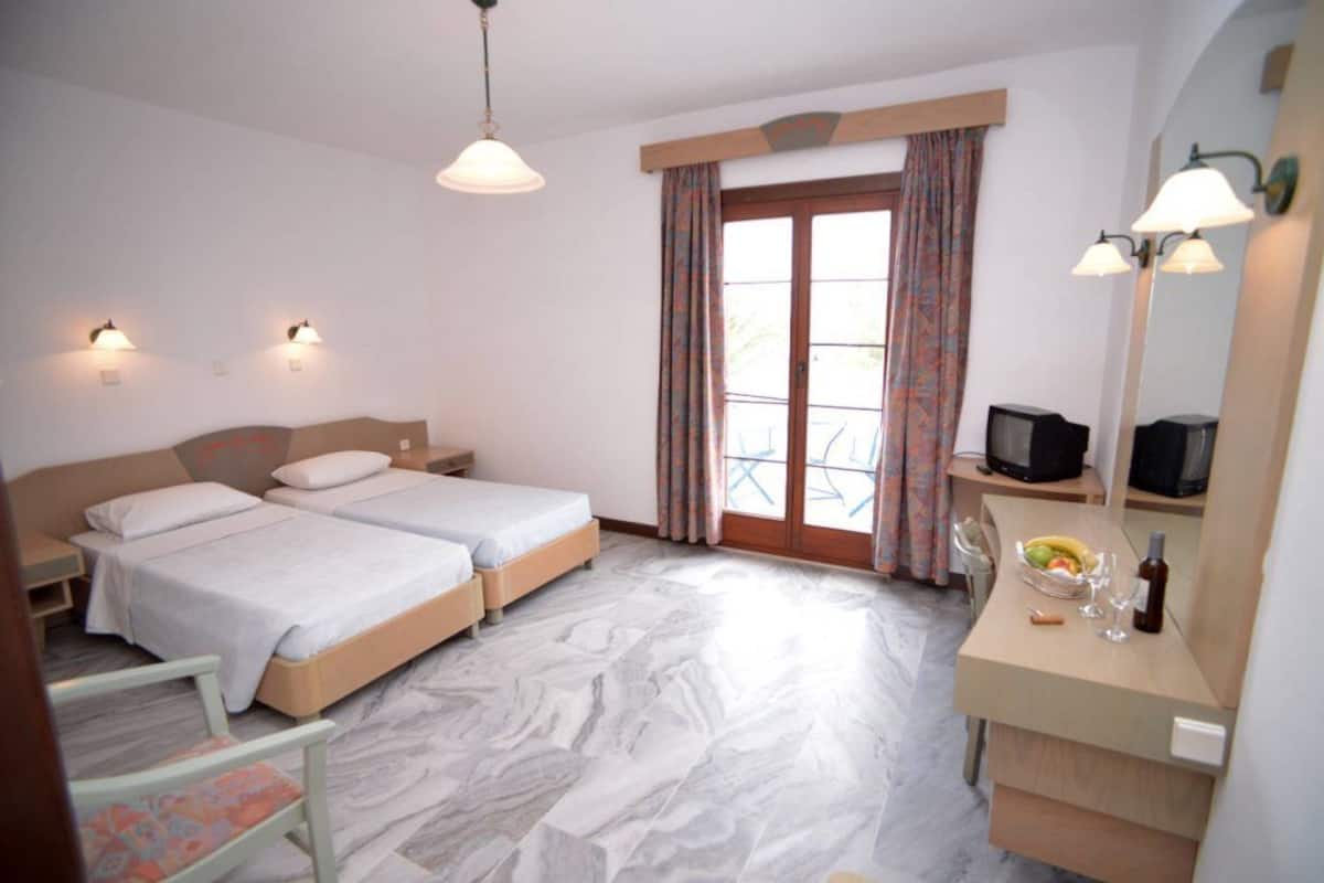 A hotel room with two beds, a desk with a TV, a mirror, and a balcony with curtains.
