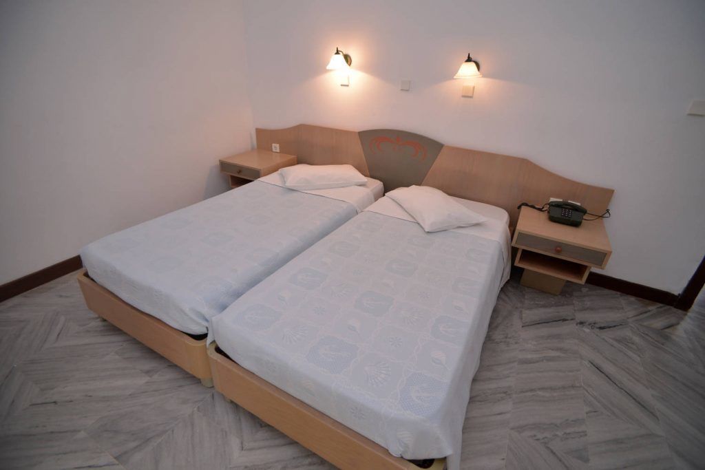 Una cama doble con cabecera, dos mesitas de noche y un teléfono sobre una de ellas.
