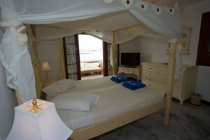 Un dormitorio con cama con dosel, televisión, mesita de noche y vistas a la playa.