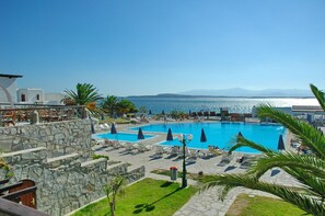 A resort pool area with multiple swimming pools, lounge chairs, and umbrellas. - Porto Paros (Paros)
