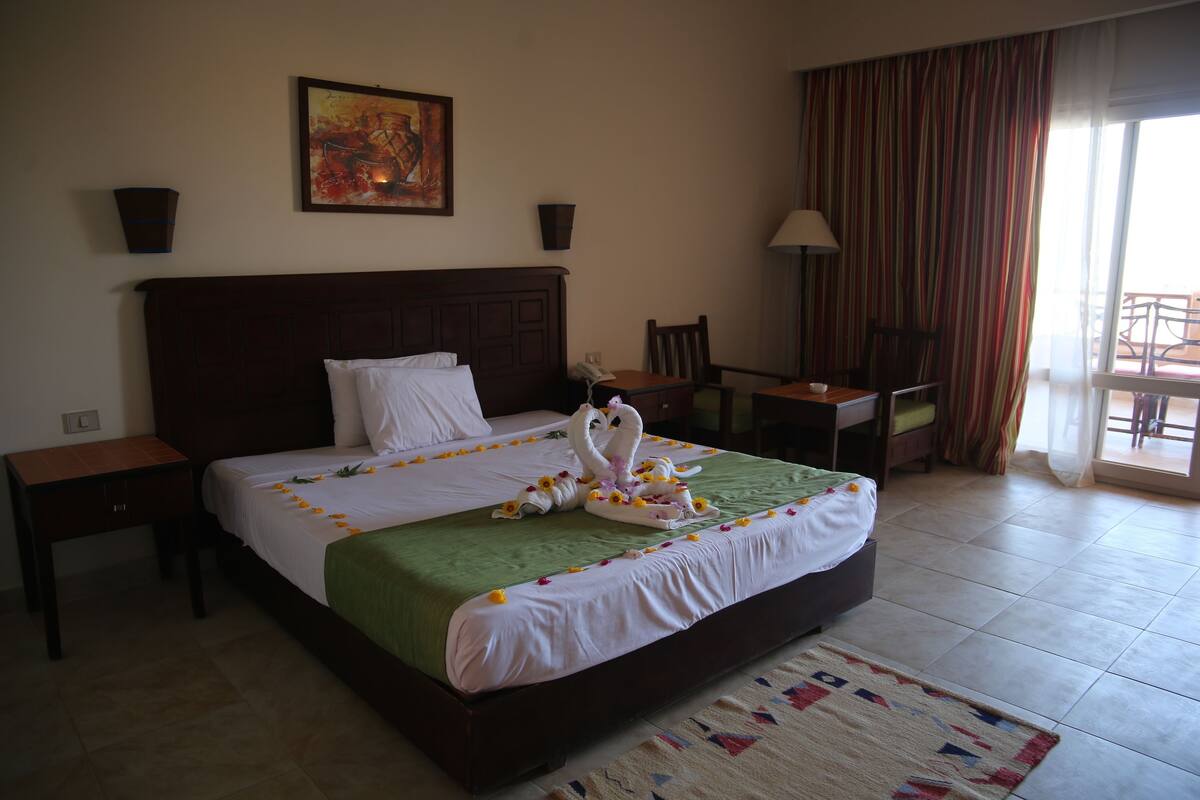 A hotel room with a large bed, a painting on the wall, a desk, and a chair.